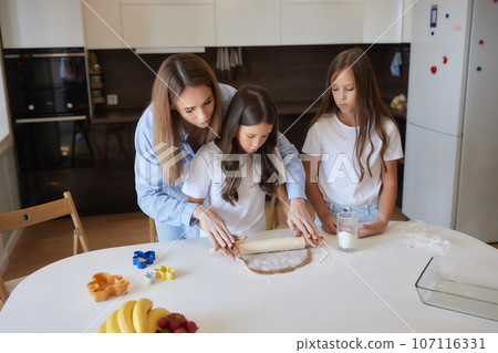 Close up image woman and little daughter knead dough with hands wooden table powdered with flour. Close up image woman and little daughter knead dough with hands wooden table powdered with flour. 107116331