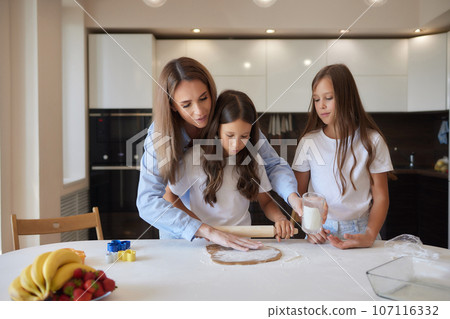 Close up image woman and little daughter knead dough with hands wooden table powdered with flour. Close up image woman and little daughter knead dough with hands wooden table powdered with flour. 107116332