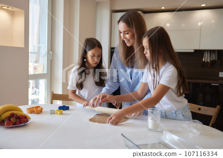 Close up image woman and little daughter knead dough with hands wooden table powdered with flour. 107116334