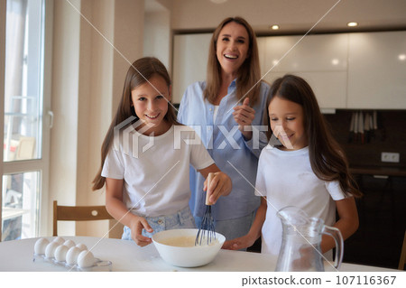 Cute little girl and her beautiful mom in aprons are playing and laughing while kneading the dough in the kitchen. Cute little girl and her beautiful mom in aprons are playing and laughing while kneading the dough in the kitchen. 107116367
