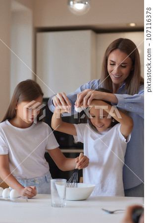 Cute little girl and her beautiful mom in aprons are playing and laughing while kneading the dough in the kitchen. Cute little girl and her beautiful mom in aprons are playing and laughing while kneading the dough in the kitchen. 107116378