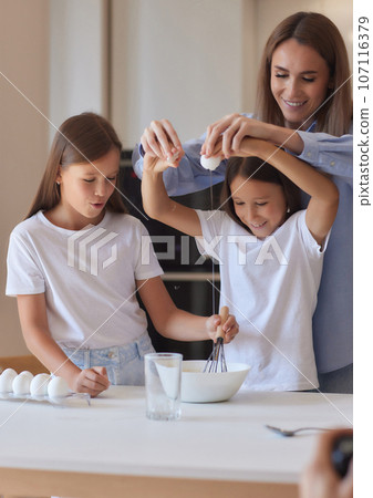 Cute little girl and her beautiful mom in aprons are playing and laughing while kneading the dough in the kitchen. Cute little girl and her beautiful mom in aprons are playing and laughing while kneading the dough in the kitchen. 107116379