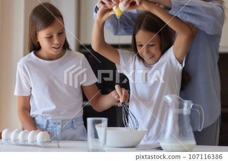 Cute little girl and her beautiful mom in aprons are playing and laughing while kneading the dough in the kitchen. Cute little girl and her beautiful mom in aprons are playing and laughing while kneading the dough in the kitchen. 107116386