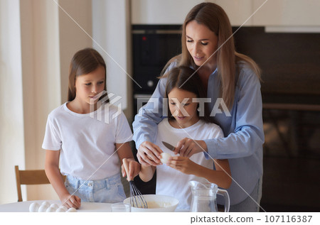 Cute little girl and her beautiful mom in aprons are playing and laughing while kneading the dough in the kitchen. Cute little girl and her beautiful mom in aprons are playing and laughing while kneading the dough in the kitchen. 107116387