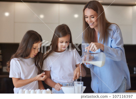 Cute little girl and her beautiful mom in aprons are playing and laughing while kneading the dough in the kitchen. Cute little girl and her beautiful mom in aprons are playing and laughing while kneading the dough in the kitchen. 107116397