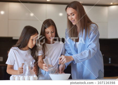 Cute little girl and her beautiful mom in aprons are playing and laughing while kneading the dough in the kitchen. Cute little girl and her beautiful mom in aprons are playing and laughing while kneading the dough in the kitchen. 107116398