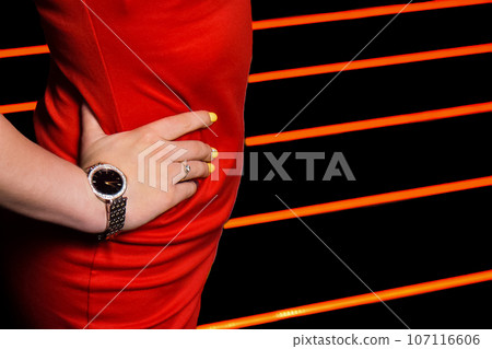 The hand of a person with a hand watch poses on the waist in a red dress, an element of a part of a woman's figure on a striped background The hand of a person with a hand watch poses on the waist in a red dress, an element of a part of a woman's figure on a striped background 107116606