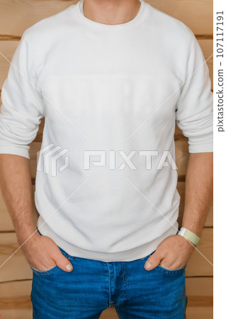 Person in white clothes, sweater, men's style, fashion and blue jeans posing with hands in pocket on wooden background 107117191