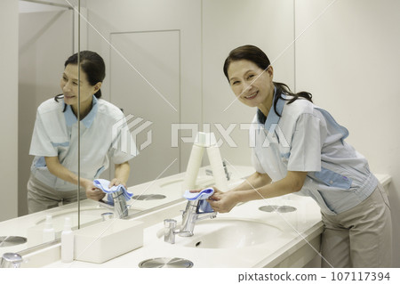 Senior female cleaner wiping down in the office washroom Senior female cleaner wiping down in the office washroom 107117394