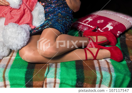 Women's slim sexy legs in flesh-colored tights and red high-heeled Louboutins on plaid vintage fabric background 107117547