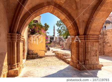 Old narrow traditional city street and minaret tower in Rhodes. 107119765