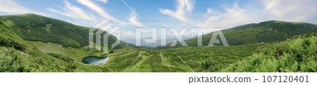 Lake on green mountains valley. Blue sky with white clouds. Rewilding and recreation concept. 107120401