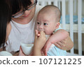 Mother holds the baby and lets her sister feed her with supplementary food 107121225