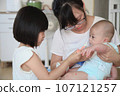 Mother holds the baby and lets her sister feed her with supplementary food 107121257
