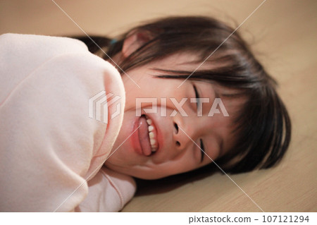 Cute Asian girl lying on the wooden floor at home smiling happily at the camera 107121294