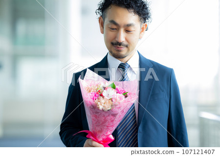 A man in a suit holding a bouquet of flowers 107121407