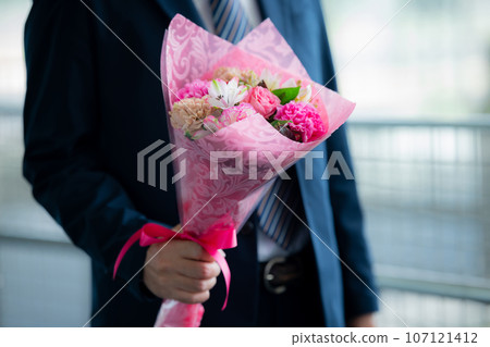 A man in a suit holding a bouquet of flowers 107121412