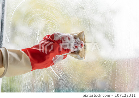 Woman cleaning window at home, closeup. Household chores. Hands with napkin cleaning window. Washing the glass on the windows with cleaning spray. Empty place for text, copy space. 107122311