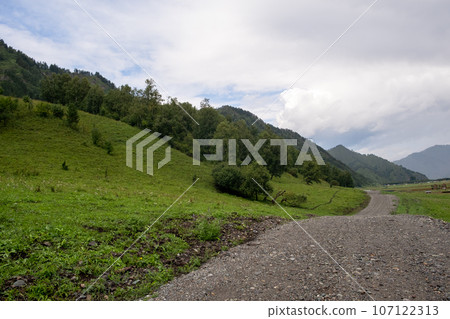 A country road between fields with hay bales in autumn in the mountains. Agricultural field with sky and clouds. The nature of agriculture. Straw in the meadow. Rural natural landscape.  107122313