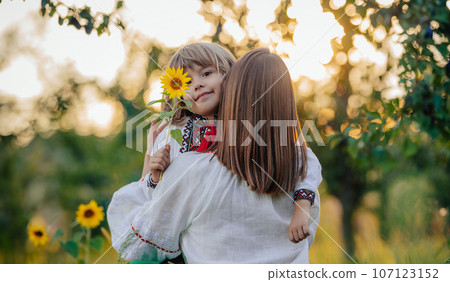 Portrait of beautiful family - 4 years old boy with sunflower, mother in garden 107123152