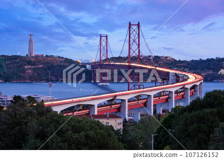 View of Lisbon view from Miradouro do Bairro do Alvito viewpoint of Tagus river, traffic with light trails on 25th of April Bridge, and Christ the King statue in the evening twilight. Lisbon, Portugal 107126152