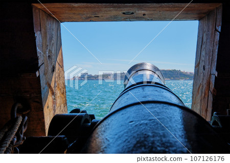 Sea view out of a gunport in hull of the ship over the gun cannon muzzle in on the gun deck of a sailing ship of Age of Sail.. Sea view out of a gunport in hull of the ship over the gun cannon muzzle in on the gun deck of a sailing ship of Age of Sail.. 107126176