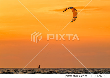 Foiling kiteboarding kitesurfing kiteboarder (kitesurfer) silhouette in the Atlantic ocean on sunset. Fonte da Telha beach, Costa da Caparica, Portugal Foiling kiteboarding kitesurfing kiteboarder (kitesurfer) silhouette in the Atlantic ocean on sunset. Fonte da Telha beach, Costa da Caparica, Portugal 107126182