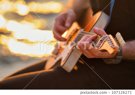 Street musician playing electric guitar hands with guitar pick close up with water in background 107126271
