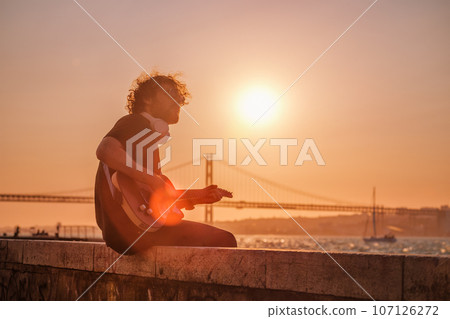Hipster street musician in black playing electric guitar in the street on sunset 107126272