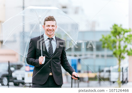 雨季/颱風雨期間拿著塑膠傘的外國商人 雨季/颱風雨期間拿著塑膠傘的外國商人 107126466