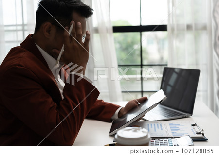 A businessman or professional person sitting stressed at work in an indoor workplaceat office job use computer laptop desk employee stressed problem corporate deadline A businessman or professional person sitting stressed at work in an indoor workplaceat office job use computer laptop desk employee stressed problem corporate deadline 107128035
