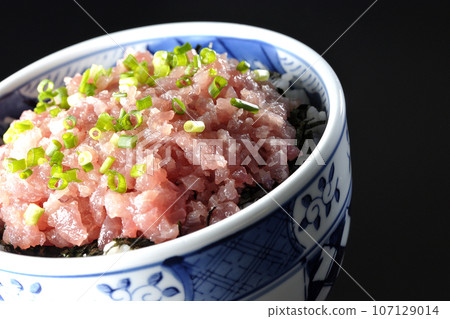 A photograph of a tuna tataki bowl topped with lots of green onions against a black background 107129014