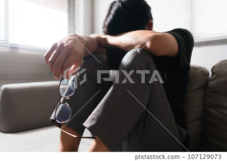 Man with mental health problem sitting on couch to resting head on his arms with depressed emotion 107129073