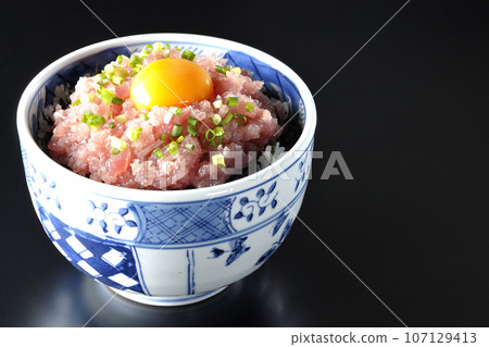 Tuna tataki bowl topped with green onion and egg yolk photographed against a black background Tuna tataki bowl topped with green onion and egg yolk photographed against a black background 107129413