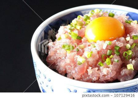 黑色背景下拍攝的鮪魚塔塔基碗,上面放著蔥和蛋黃 黑色背景下拍攝的鮪魚塔塔基碗,上面放著蔥和蛋黃 107129416