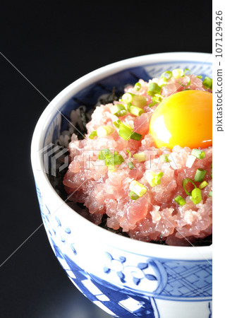 Tuna tataki bowl topped with green onion and egg yolk photographed against a black background Tuna tataki bowl topped with green onion and egg yolk photographed against a black background 107129426