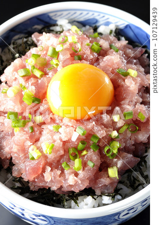 An overhead shot of a tuna tataki bowl topped with green onions and egg yolk against a black background 107129439