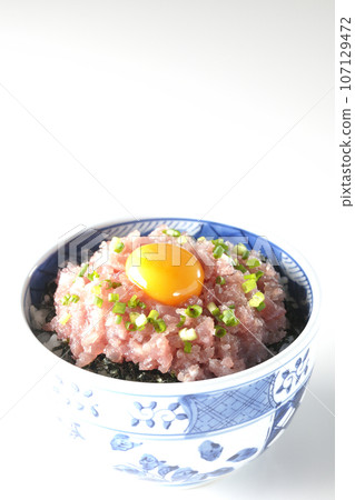 Tuna tataki bowl topped with green onion and egg yolk photographed against a white background 107129472