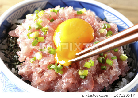 Crack the egg for the tuna tataki bowl topped with green onion and egg yolk. 107129517