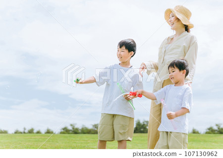 Mom, boy, brother, and child playing with soap bubble sticks in the grassland/park Mom, boy, brother, and child playing with soap bubble sticks in the grassland/park 107130962