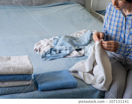 Woman folding clean terry towel in the bedroom. Organizing laundry at home. 107131141