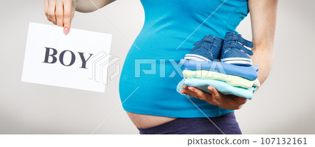 Pregnant woman holding card with inscription boy and clothes for newborn Pregnant woman holding card with inscription boy and clothes for newborn 107132161