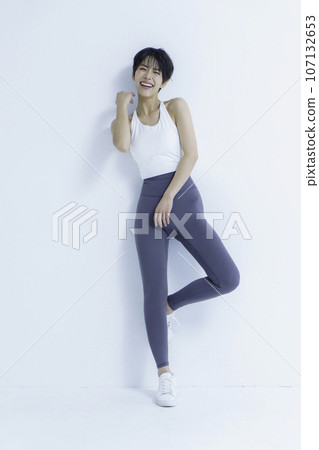 Portrait of a young woman wearing yoga wear against a white background, vertical position 107132653