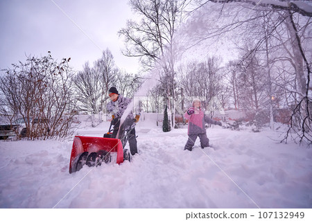 A young man clears snow with a snow blower in his yard. A young man clears snow with a snow blower in his yard. 107132949