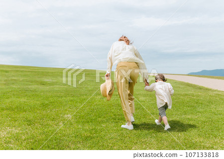 Back view of a mother and child walking hand in hand through a meadow or park 107133818