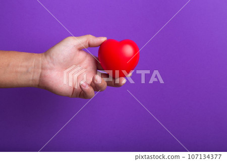 Hand with red heart on purple background. 107134377