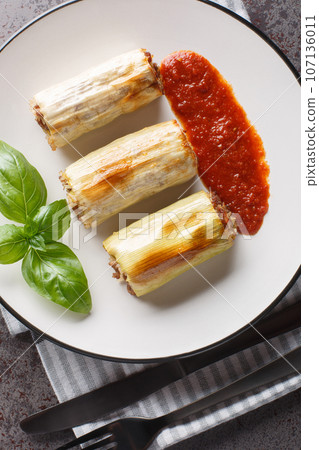 Leek dolma stuffed with minced meat, rice, cheese and vegetables served with tomato sauce close-up in a plate on the table. Vertical top view Leek dolma stuffed with minced meat, rice, cheese and vegetables served with tomato sauce close-up in a plate on the table. Vertical top view 107136011