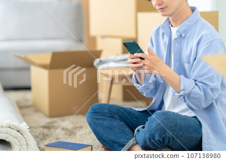 Body parts of a young man packing for moving while looking at his smartphone Body parts of a young man packing for moving while looking at his smartphone 107138980