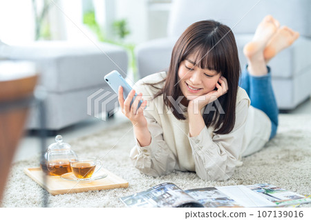 A young woman relaxing in the living room while looking at her smartphone 107139016
