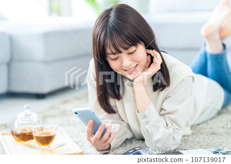 A young woman relaxing in the living room while looking at her smartphone 107139017